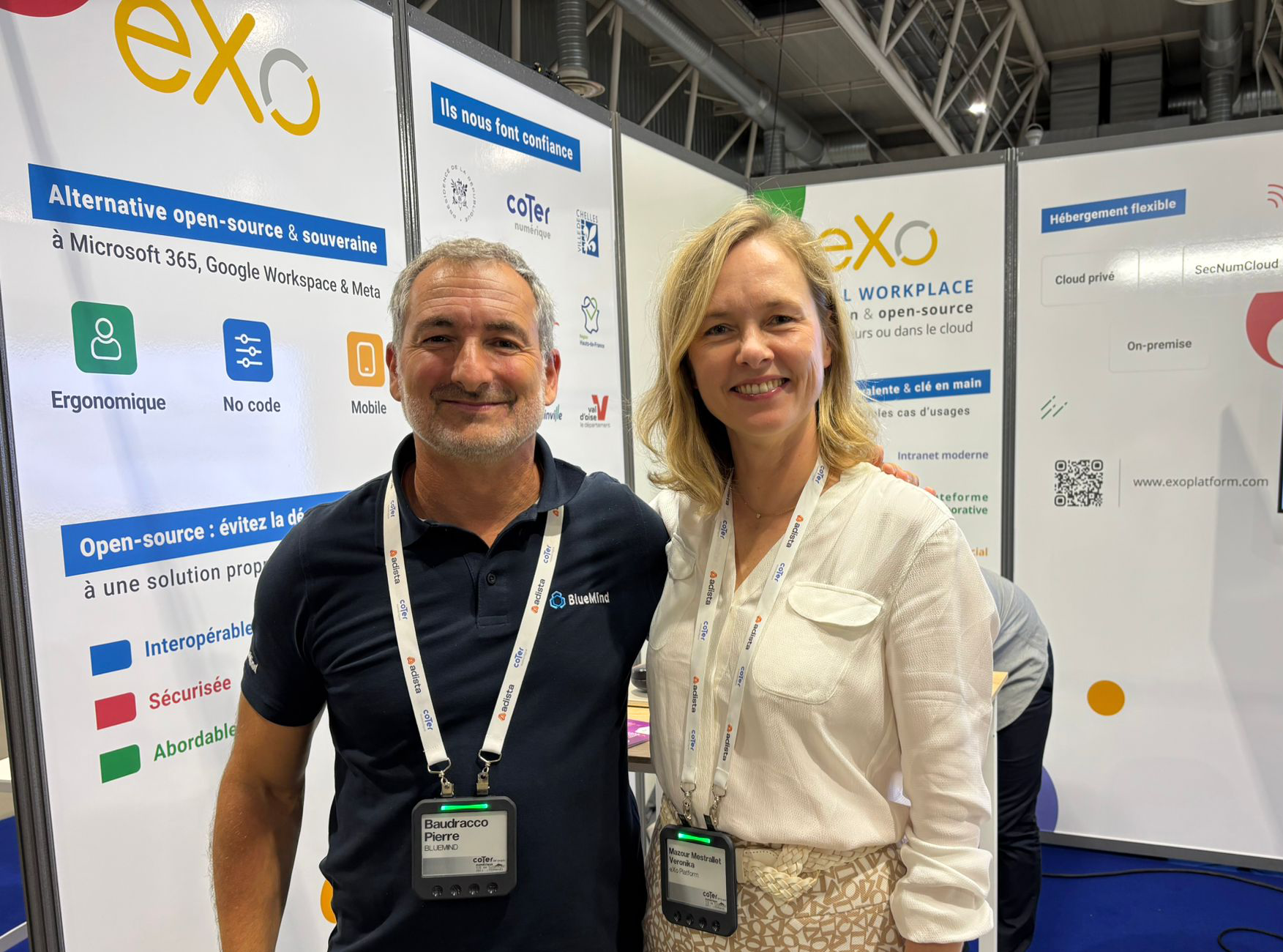 Pierre Baudracco on the left and Veronika Mazour Mestrallet on the right, standing and smiling in front of the eXo booth during the CoTer 2025 event.